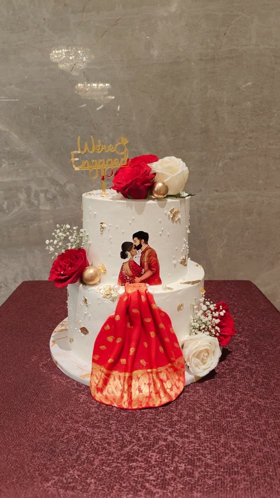 Two-tier engagement cake with a hand-painted couple and a red saree drape