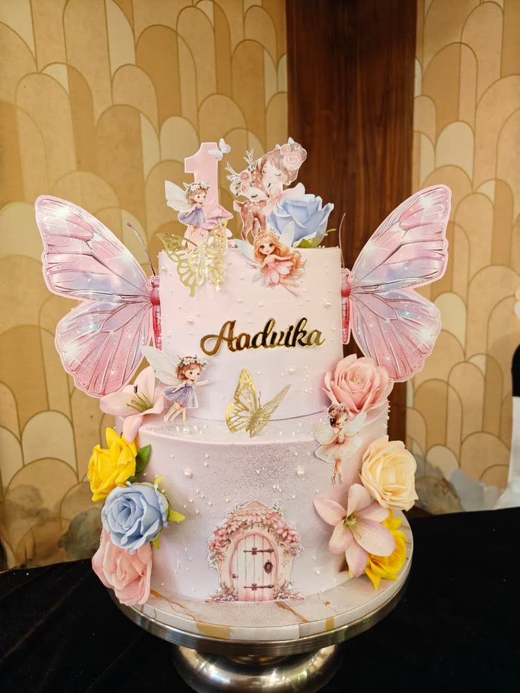 Two-tier pink fairy-garden first-birthday cake with butterfly wings and roses