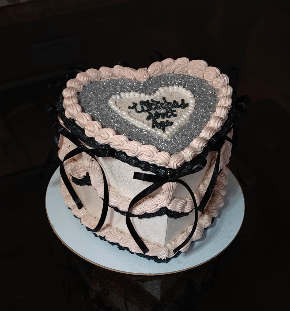 Heart-shaped vintage cake in blush pink with black ribbon bows and silver glitter