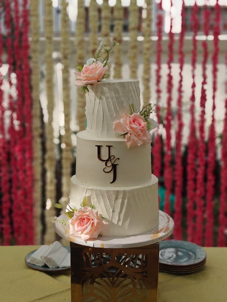 Three-tier textured white wedding cake with a monogram and peach roses