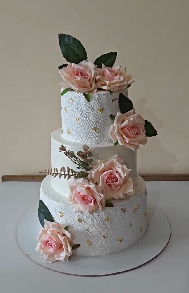 Three-tier white textured cake with gold leaf and peach roses