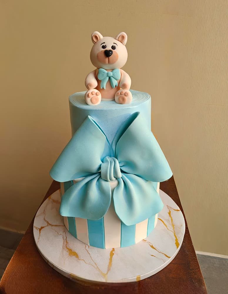 Baby-blue cake with a large fondant bow and a teddy bear on top